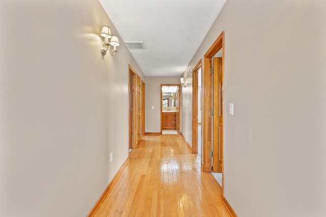 hall featuring light wood-style flooring, visible vents, and baseboards