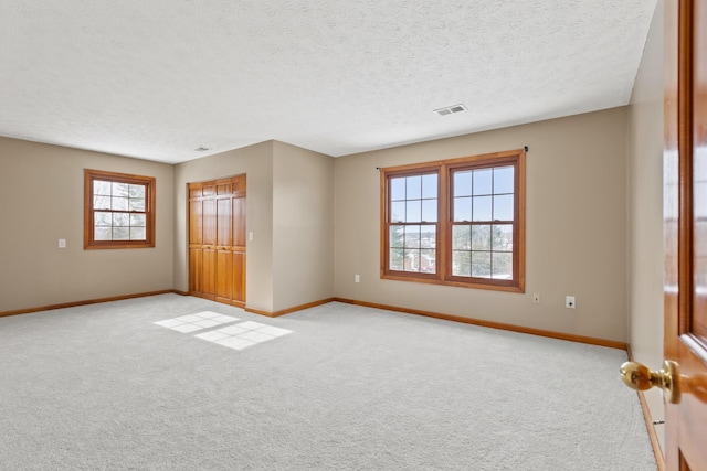 unfurnished bedroom with a closet, light colored carpet, visible vents, a textured ceiling, and baseboards