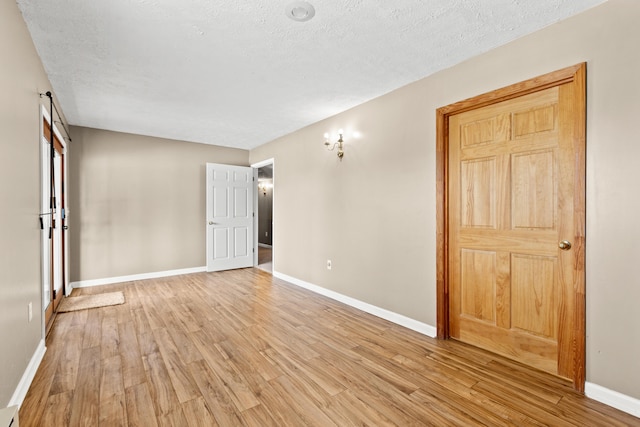 empty room featuring light wood-style floors, baseboards, and a textured ceiling