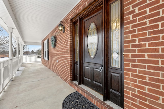 doorway to property with a porch and brick siding