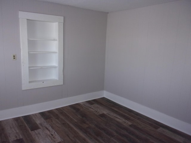 unfurnished room featuring dark wood-type flooring and built in shelves