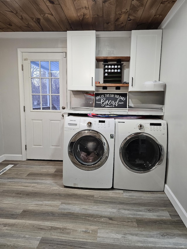 washroom featuring cabinet space, baseboards, wooden ceiling, wood finished floors, and washing machine and dryer