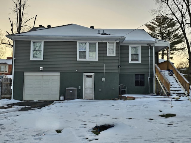 snow covered property with central AC unit and a garage