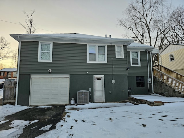 snow covered rear of property with stairs, stucco siding, a garage, and central AC unit