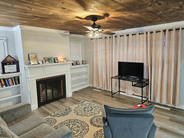 living area featuring a brick fireplace, wooden ceiling, ceiling fan, and wood finished floors