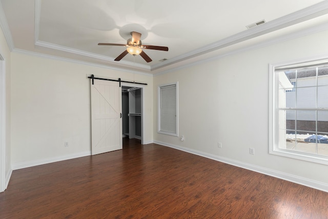 empty room featuring dark wood-type flooring, ceiling fan, ornamental molding, and a barn door