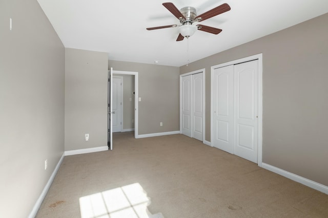 unfurnished bedroom with light carpet, two closets, and ceiling fan