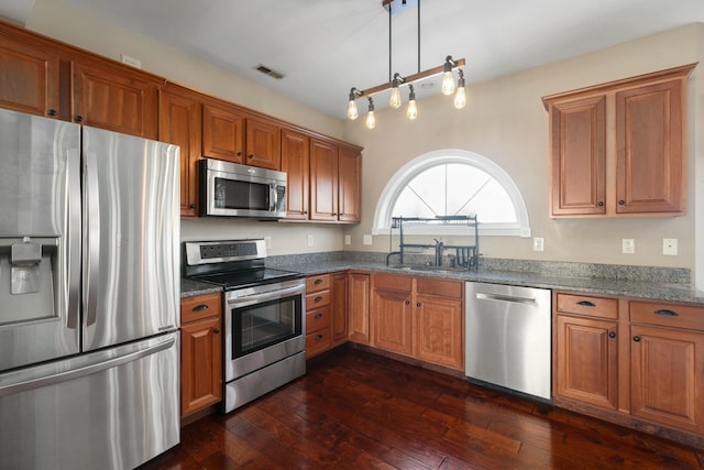 kitchen featuring stainless steel appliances, dark wood-type flooring, pendant lighting, and dark stone counters