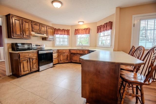 kitchen featuring sink, a kitchen breakfast bar, light tile patterned floors, electric range, and kitchen peninsula