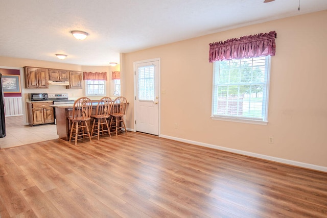 kitchen with stainless steel electric range oven, plenty of natural light, light wood-type flooring, and a kitchen breakfast bar