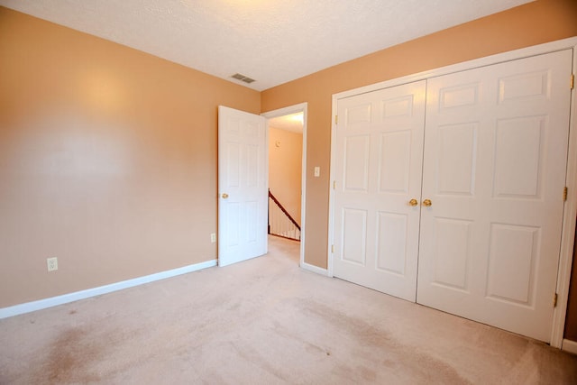 unfurnished bedroom with light colored carpet, a closet, and a textured ceiling