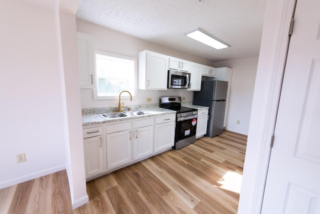 kitchen with light wood-type flooring, a sink, appliances with stainless steel finishes, white cabinets, and light countertops