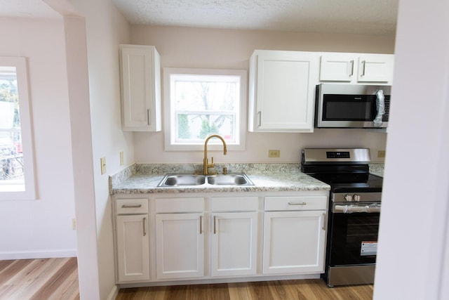 kitchen featuring light wood-style flooring, appliances with stainless steel finishes, white cabinetry, and a sink