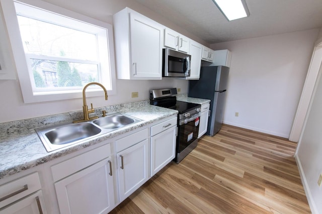 kitchen with light wood finished floors, a sink, stainless steel appliances, light countertops, and white cabinets