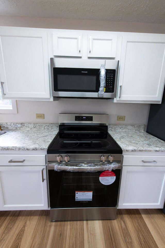 kitchen featuring light stone countertops, light wood-type flooring, stainless steel appliances, a textured ceiling, and white cabinetry