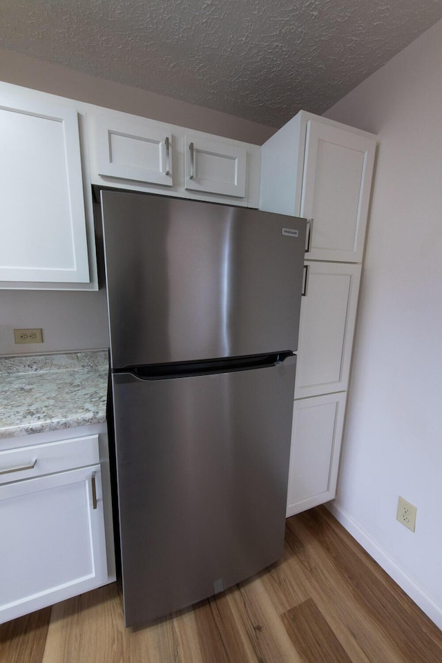 kitchen with a textured ceiling, white cabinetry, freestanding refrigerator, and light wood-style floors