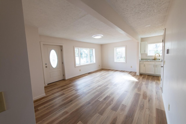 foyer entrance featuring light wood-style flooring, a textured ceiling, and baseboards