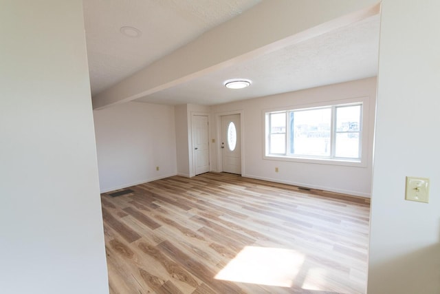 foyer featuring light wood-style flooring, beamed ceiling, and baseboards