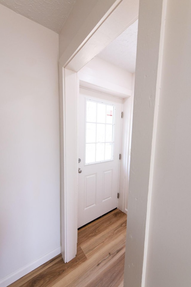 doorway to outside featuring baseboards, light wood-style floors, and a textured ceiling