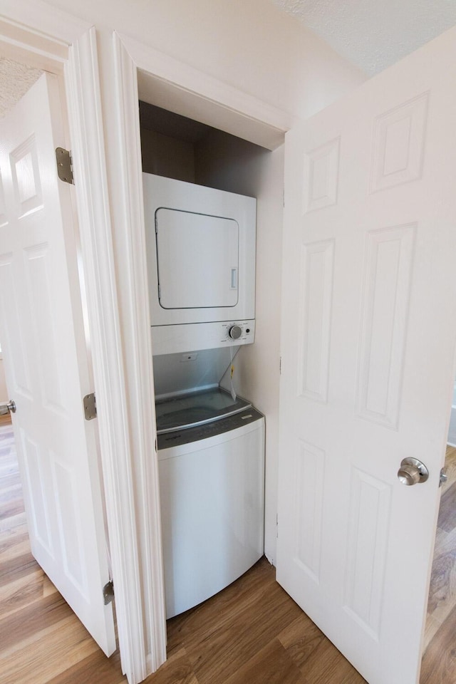 laundry area with laundry area, stacked washer and dryer, and wood finished floors