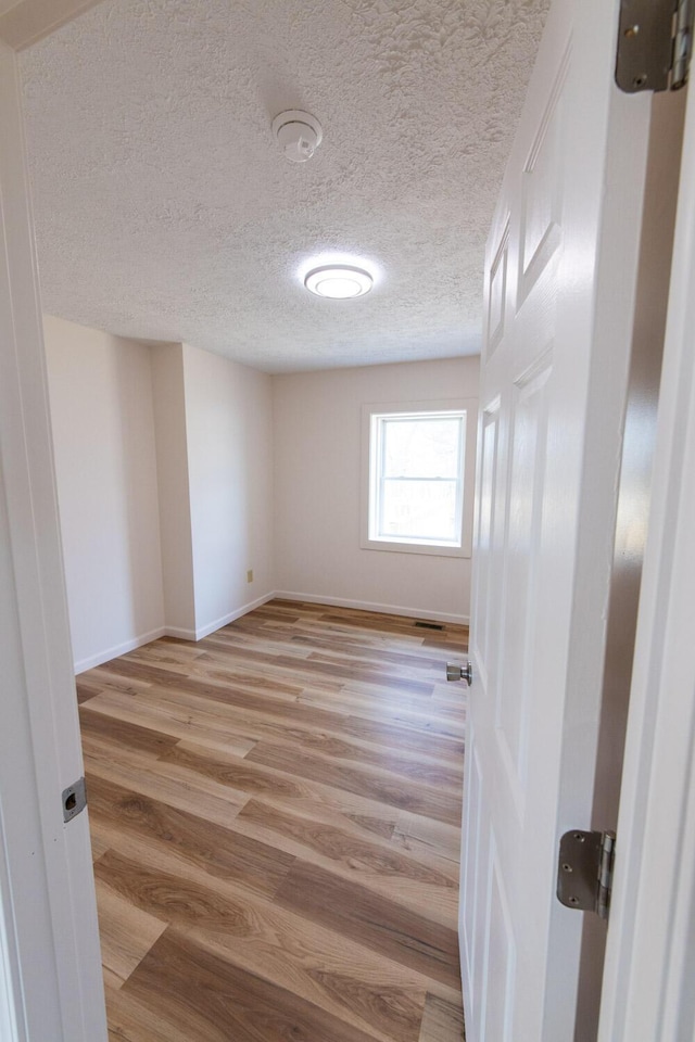 unfurnished room with visible vents, baseboards, light wood-type flooring, and a textured ceiling