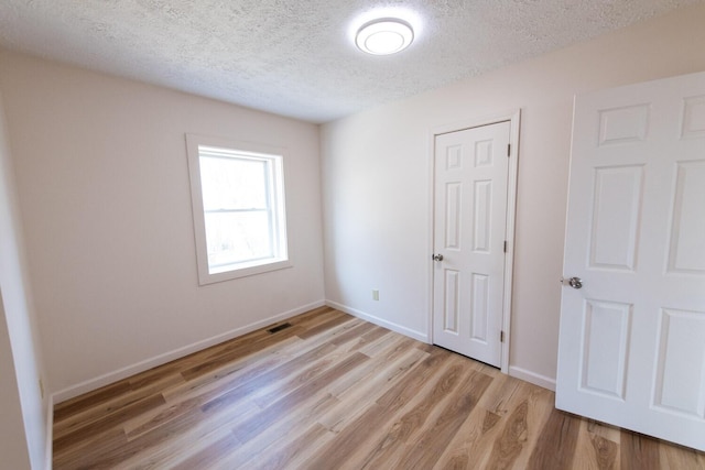 unfurnished bedroom with light wood-type flooring, baseboards, a textured ceiling, and visible vents