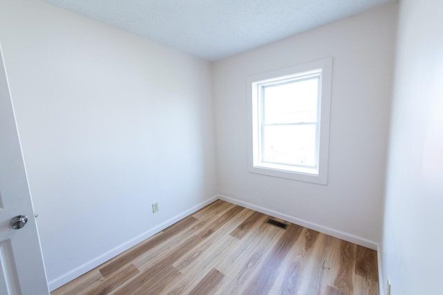 empty room featuring baseboards, visible vents, and light wood finished floors