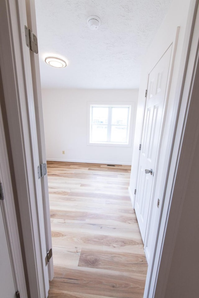 hallway featuring baseboards, light wood finished floors, and a textured ceiling