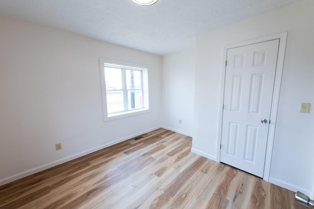 unfurnished bedroom with a textured ceiling, baseboards, and wood finished floors