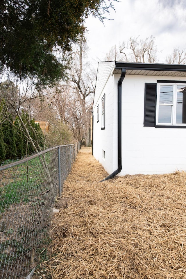 view of side of home featuring concrete block siding and fence