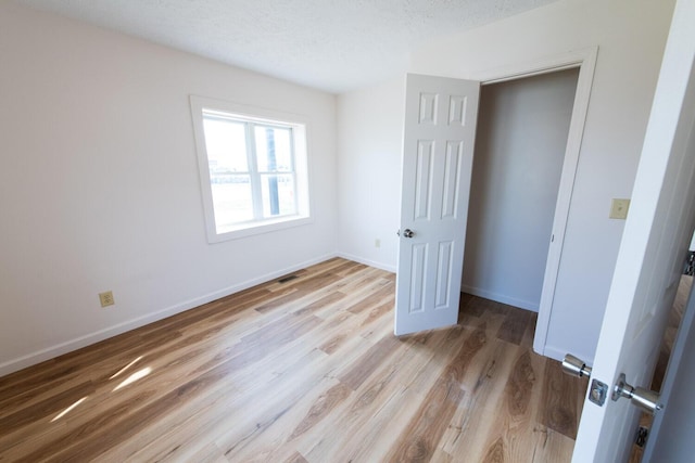 unfurnished bedroom featuring visible vents, a textured ceiling, baseboards, and light wood-style floors