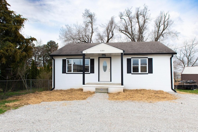 view of front facade featuring a shingled roof, concrete block siding, and fence