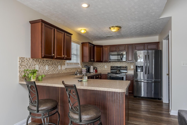 kitchen featuring decorative backsplash, a kitchen breakfast bar, appliances with stainless steel finishes, and kitchen peninsula