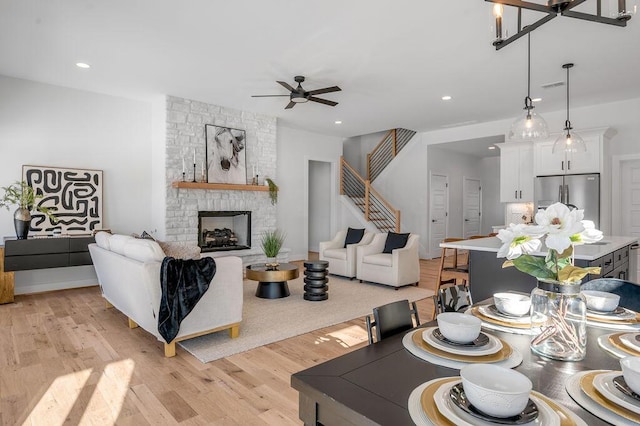 living room featuring light wood-type flooring, ceiling fan, and a stone fireplace