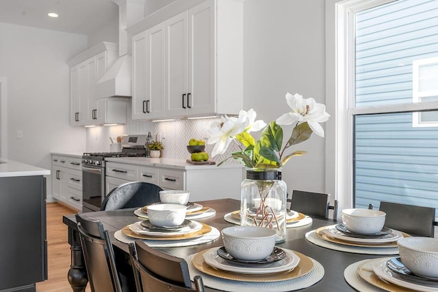 kitchen featuring light hardwood / wood-style floors, stainless steel range with gas stovetop, backsplash, wall chimney range hood, and white cabinets