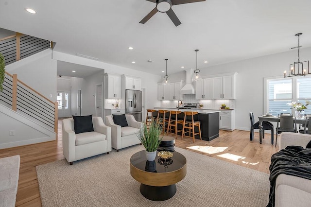 living room with sink, ceiling fan with notable chandelier, and light hardwood / wood-style floors