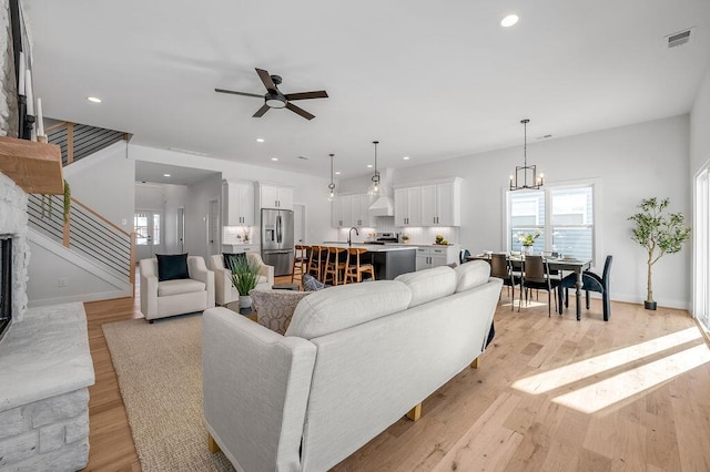 living room featuring light wood-type flooring, sink, and ceiling fan with notable chandelier