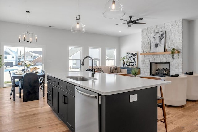 kitchen with ceiling fan with notable chandelier, a kitchen island with sink, a fireplace, stainless steel dishwasher, and sink