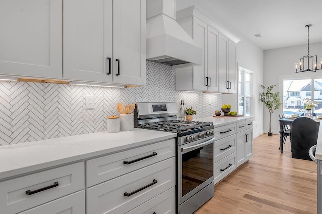 kitchen featuring decorative light fixtures, premium range hood, stainless steel range with gas cooktop, white cabinets, and a chandelier