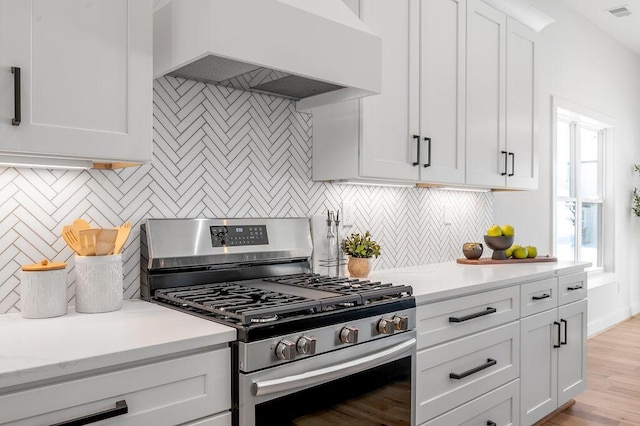 kitchen featuring custom exhaust hood, white cabinets, gas range, and tasteful backsplash