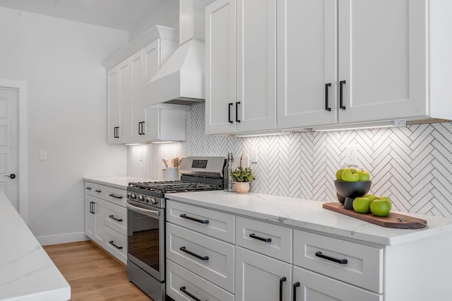 kitchen featuring white cabinetry, wall chimney exhaust hood, stainless steel gas stove, and light stone countertops