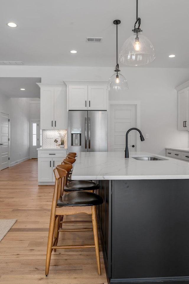 kitchen featuring pendant lighting, stainless steel refrigerator with ice dispenser, white cabinetry, light hardwood / wood-style floors, and sink