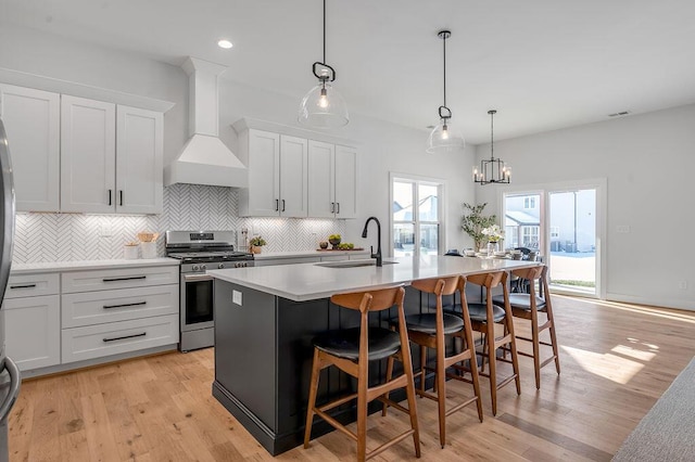 kitchen with a center island with sink, white cabinets, gas stove, and custom range hood