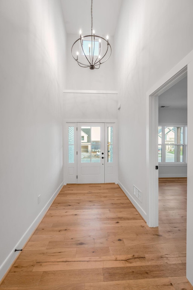 foyer entrance with an inviting chandelier, a towering ceiling, and light hardwood / wood-style flooring