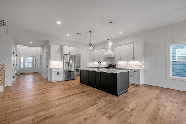 kitchen featuring decorative light fixtures, white cabinets, stainless steel appliances, and a kitchen island with sink