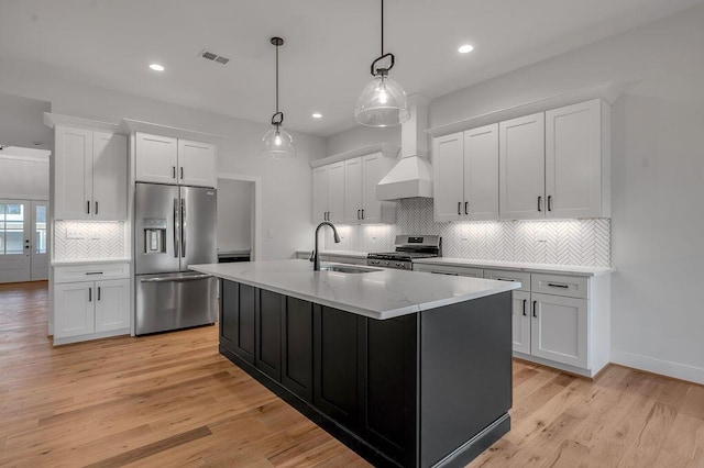 kitchen featuring a center island with sink, appliances with stainless steel finishes, white cabinets, and decorative light fixtures