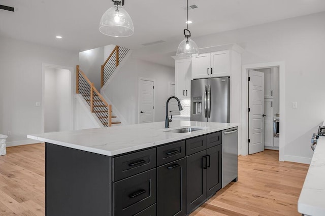 kitchen with sink, hanging light fixtures, a kitchen island with sink, stainless steel appliances, and white cabinets