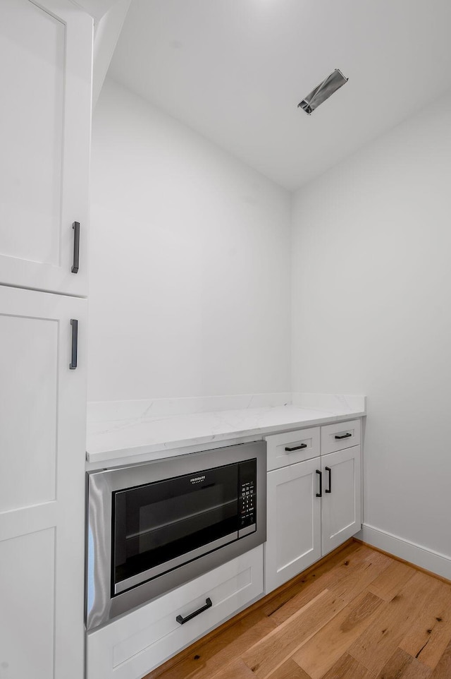 interior details with light hardwood / wood-style floors, light stone countertops, white cabinets, and black microwave