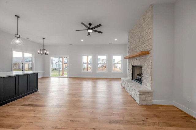 unfurnished living room with ceiling fan with notable chandelier, light hardwood / wood-style floors, and a stone fireplace