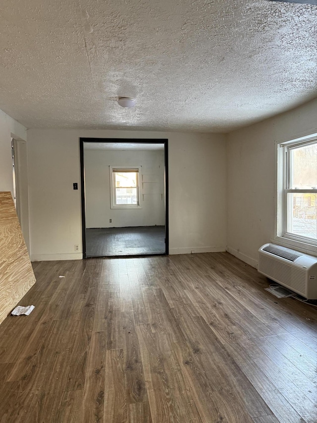 unfurnished living room featuring a textured ceiling, plenty of natural light, hardwood / wood-style floors, and a wall mounted air conditioner